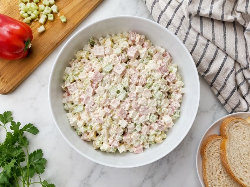 Creamy  with chopped celery, pickles, and fresh herbs in a white bowl.