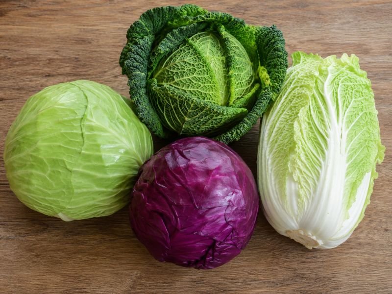 Fresh green, savoy, napa, and red cabbages arranged on a wooden surface, showing different cabbage varieties suitable for boiling.