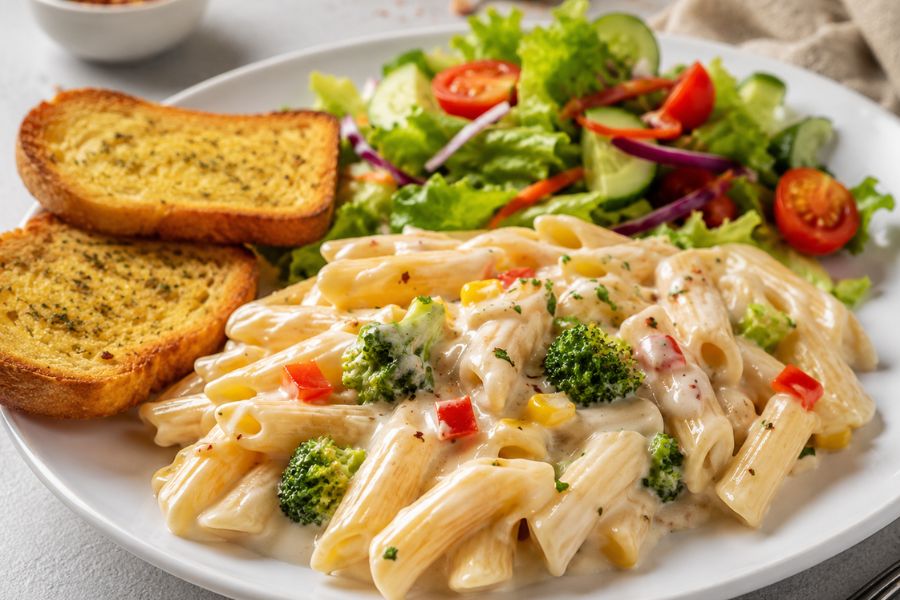 white sauce pasta served with garlic bread and salad