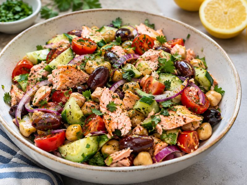 Mediterranean salmon salad with cucumber, tomatoes, chickpeas, red onion, parsley, and olives in a bowl.
